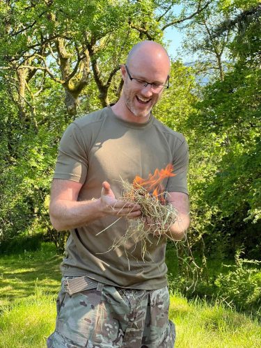 A man holding some hays with fire during their wild camping stag do in Cardiff