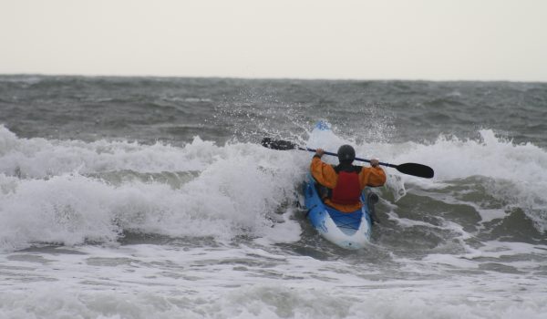 A person doing surf kayaking in the ocean.